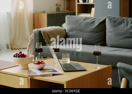 Computer portatile e bicchieri di vino rosso disposti sul tavolino da caffè nel soggiorno Foto Stock