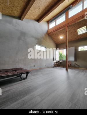 Interni moderni - design rustico-industriale che si fonde con travi in legno a vista, soffitto alto, pareti in cemento, pavimenti in legno scuro e grandi finestre. Foto Stock
