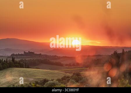 Il tramonto toscano bagna le colline ondulate e un castello lontano dalla luce dorata Foto Stock