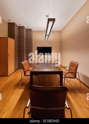 Il capo del tavolo è seduto nella sala riunioni in toni caldi. Vista simmetrica di una moderna sala conferenze con pareti beige, sedie abbronzanti e tavolo marrone Foto Stock