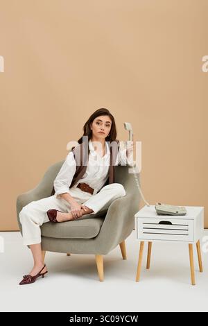 Una giovane donna alla moda con lunghi capelli marroni si rilassa mentre tiene un telefono vintage in uno studio. Foto Stock
