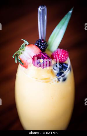 Primo piano del frullato di mango in vetro con cucchiaio e guarnizione di frutta Foto Stock