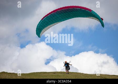 Vista di un parapendio con un colorato paracadute che si innalza su uno sfondo di soffici nuvole bianche e cielo azzurro, Oderen, Grand Est, Francia. Foto Stock