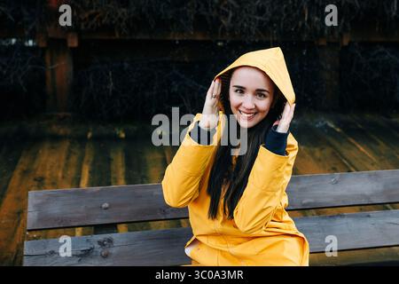 Donna sorridente in impermeabile giallo seduta sulla panchina Foto Stock
