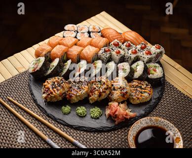 Sushi assortiti disposti su un piatto di ardesia, con una varietà di panini, nigiri e wasabi, accompagnati da bacchette Foto Stock