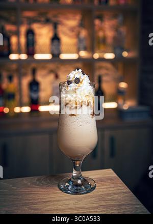 Rinfrescante frappè di caffè ghiacciato condito con panna montata, chicchi di caffè e goccioline di caramello, servito in un elegante bicchiere su un bancone del bar Foto Stock