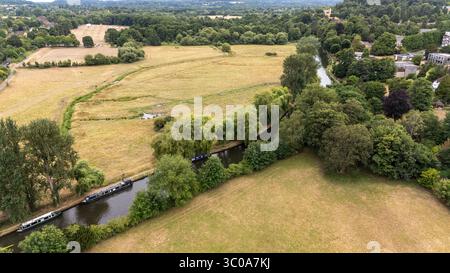 Vista aerea di un tranquillo canale che serpeggia attraverso i lussureggianti campi di Guildford e le rive alberate, riflettendo la luce soffusa del cielo, Guildford, Inghilterra, Regno Unito. Foto Stock
