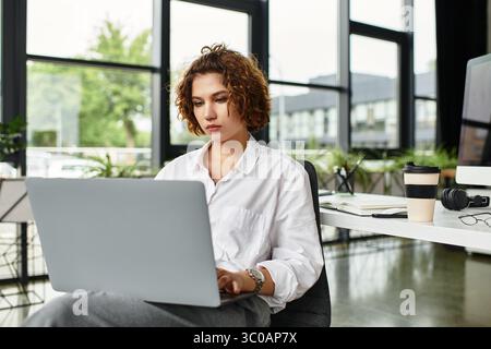 La giovane donna d'affari dai capelli ricci si impegna con il suo notebook in un ufficio moderno. Foto Stock