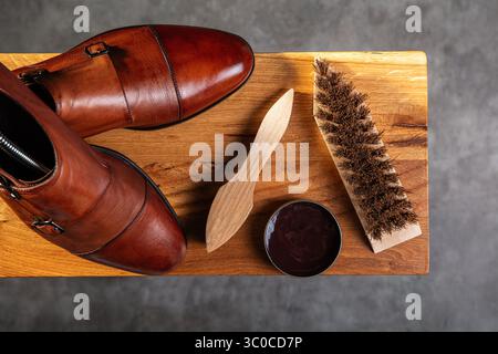 Vista dall'alto di un paio di scarpe in pelle marrone lucida posizionate accanto a una spazzola per scarpe in legno, un applicatore per lucidatura e uno stagno aperto di lucidatura marrone su una Foto Stock