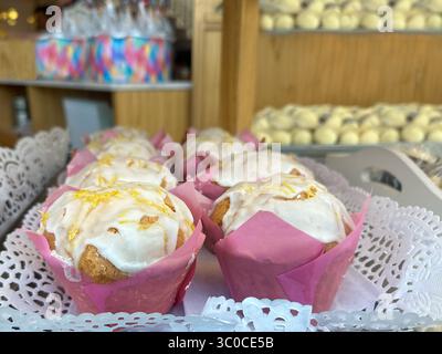 muffin appena sfornati in fodere rosa per cupcake, con altri prodotti da forno assortiti offuscati sullo sfondo. I toni caldi e la messa a fuoco delicata suggeriscono un ambiente accogliente Foto Stock