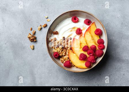 Ciotola di muesli con yogurt greco, pesca, lampone e miele. Colazione sana bilanciata con yogurt proteico, frutta estiva e frutti di bosco. Vista dall'alto. Foto Stock