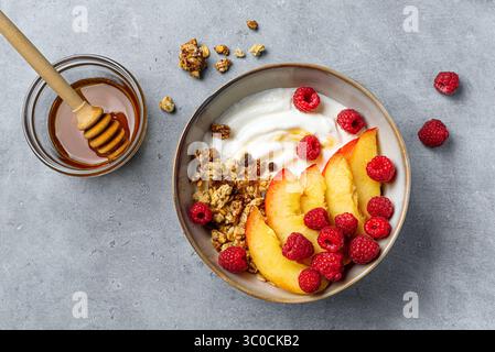 Ciotola di muesli con yogurt greco, pesca, lampone e miele. Colazione sana bilanciata con yogurt proteico, frutta estiva e frutti di bosco. Vista dall'alto. Foto Stock