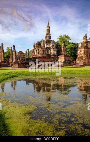 Splendida vista verticale del tempio di Wat Mahathat riflessa in uno stagno e cielo blu nel Parco storico di Sukhothai, Thailandia Foto Stock