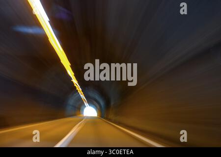 Guarda dall'auto mentre guidi velocemente su un pilota che sta accelerando attraverso un lungo tunnel con tunnel dritto con luce alla fine di un lungo percorso Foto Stock