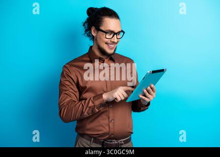 Un giovane uomo sicuro di sé utilizza un tablet su uno sfondo blu brillante per motivi di lavoro e di stile di vita Foto Stock
