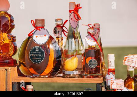 1 giugno 2025, Belgrado, Serbia: Varie bottiglie di brandy alla frutta e liquori, esposte su una bancarella di legno in un mercato locale Foto Stock