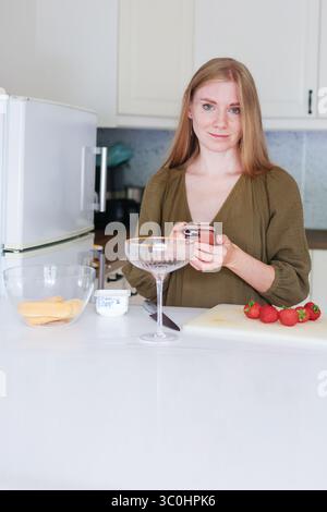 Donna che prepara dessert alle fragole in una cucina moderna, preparazione di dolcetti fatti in casa. Foto Stock