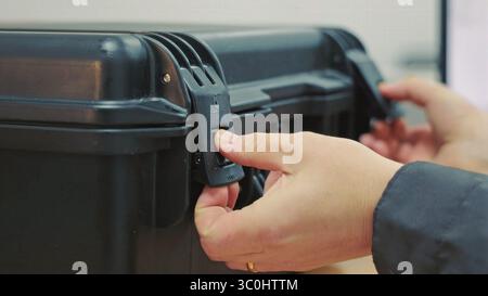 Mani che aprono un fermo nero della custodia. Vista ravvicinata delle mani che sbloccano un fermo su una robusta custodia nera. Foto Stock