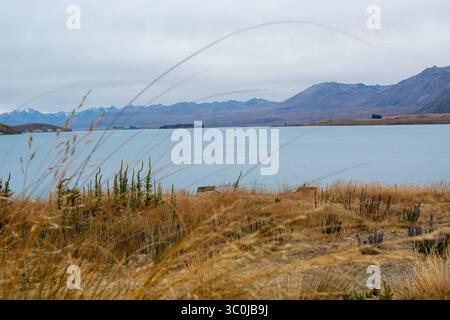 Un tranquillo paesaggio caratterizzato da un lago calmo circondato da montagne e prati erbosi. Il cielo è coperto, creando un'atmosfera tranquilla. Foto Stock