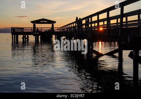 Tramonto dietro un molo di legno sagomato, con riflessi e increspature sull'acqua, Davis Bay, Sunshine Coast Highway, Sechelt Foto Stock