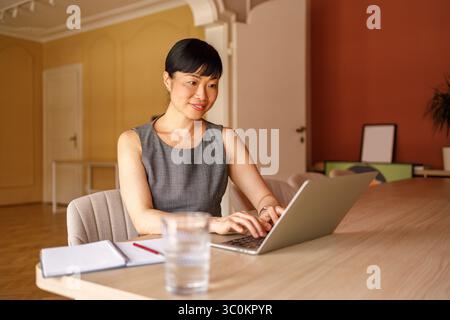 Ritratto di una donna d'affari di medie dimensioni che analizza i rapporti su un computer portatile mentre lavora alla scrivania in ufficio Foto Stock