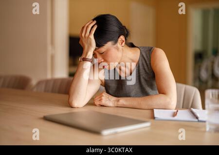 Donna d'affari stanca con la testa in mano che dorme alla scrivania stanca e lo stress sopraffatto dal carico di lavoro dell'ufficio aziendale Foto Stock