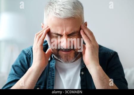 Uomo anziano che ha mal di testa, toccando i suoi templi Foto Stock