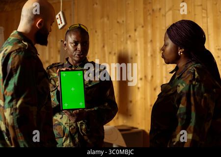 Soldati in tiro guardano video su un tablet con schermo isolato progettato per migliorare le capacità di tiro. Unità militari che cercano un dispositivo di mockup per imparare a usare al meglio le armi per attaccare i bersagli Foto Stock