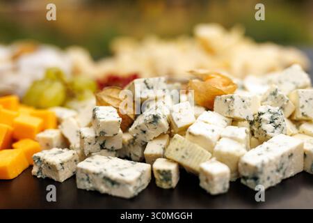 Primo piano di formaggi assortiti a cubetti su un piatto, tra cui formaggio blu, cheddar e uva. Colorato servizio gourmet. Foto Stock