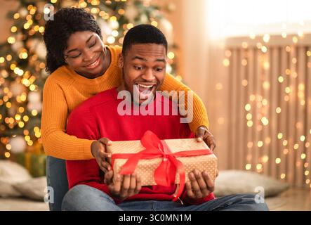 Sorpreso africano americano giovane marito tenere scatola con dono e. nastro rosso Foto Stock