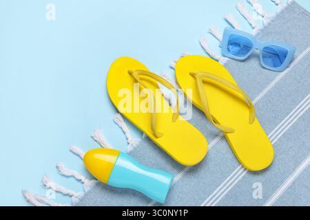 Composizione con eleganti scarpe da spiaggia, asciugamano e bottiglia di crema solare su sfondo blu, primo piano Foto Stock