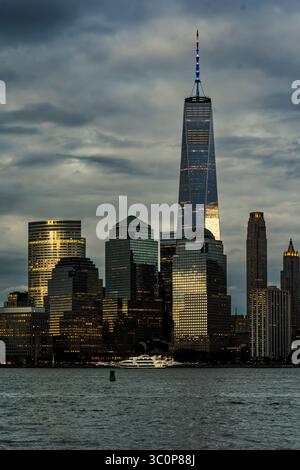 Jersey City, New Jersey - US - 19 luglio 2025 al crepuscolo, l'One World Trade Center si illumina nello skyline di Lower Manhattan, incorniciato da nuvole spettacolari e scintillanti Foto Stock