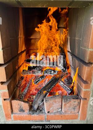 Fiamme e braci incandescenti in un caminetto in mattoni con tronchi di legno in fiamme per barbecue Foto Stock