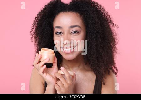 Bella donna brasiliana con barattolo di crema di collagene su sfondo rosa Foto Stock