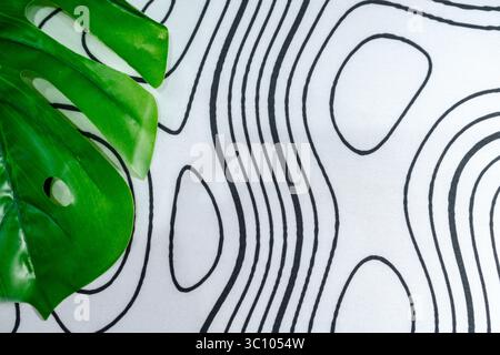 Superficie in tessuto con linee di contorno nere astratte e foglie verdi tropicali. Perfetto per lo sfondo, i mockup o il moderno design visivo con la natura. Foto Stock