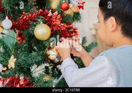 Baby boy standing beside Christmas tree at home. Selective focus, back view. Foto Stock