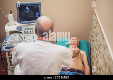 Uomo anziano che ha un esame medico. Il paziente anziano sta effettuando un esame ecografico del suo cuore da parte di un medico esperto. Foto Stock