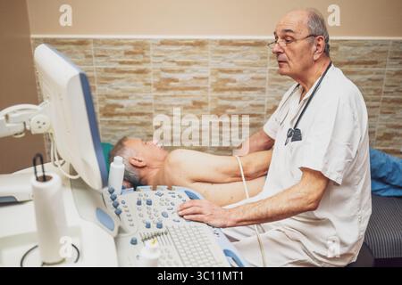 Uomo anziano che ha un esame medico. Il paziente anziano sta effettuando un esame ecografico del suo cuore da parte di un medico esperto. Foto Stock