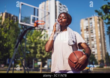 La giovane donna nera è in piedi sul campo da basket. Lei è stanca e spazza via il sudore dal viso. Foto Stock