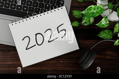 Notebook a spirale 2025 con laptop su scrivania in legno, rendering 3D. Foto Stock