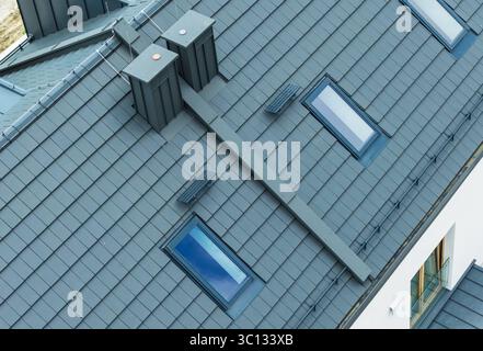 Vista ravvicinata di un moderno tetto residenziale con lucernari, sistemi di ventilazione e piastrelle eleganti in condizioni di luce naturale. Foto Stock