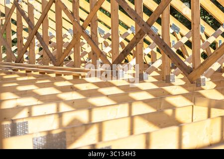 I lavoratori stanno costruendo una struttura in legno per una casa, mostrando travi e supporti sotto il sole, evidenziando la struttura intricata e le ombre Foto Stock