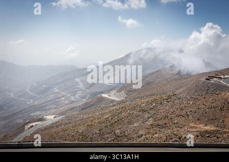 Catena montuosa di Jebel Jais a Ras al Khaimah, Emirati Arabi Uniti, con tortuosa strada asfaltata e parcheggio lungo la strada, montagne rocciose di Hajar, Emirati Arabi Uniti. Foto Stock