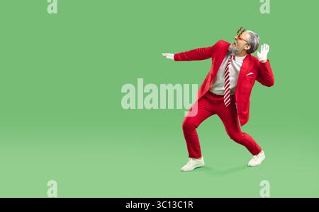 Foto orizzontale di un uomo gioioso vestito con una tuta rossa come Babbo Natale, balla e divertiti Foto Stock