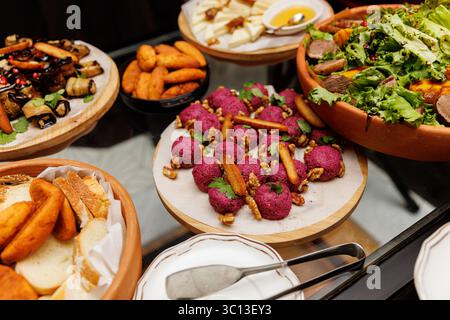 Ampia scelta di antipasti freddi, tra cui palline di barbabietola con noci, involtini di melanzane, insalata e piatto di formaggi. Esposto su piastre in legno e ceramica. Foto Stock