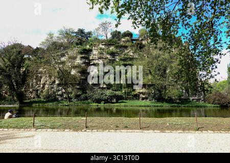 Coppia che guarda oltre l'acqua alla formazione rocciosa artificiale, belvedere, a Parc Buttes Chaumont, Parigi, Francia. Foto Stock