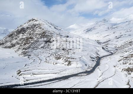 La vista aerea di un fiume tortuoso scolpisce il suo percorso attraverso un paesaggio incontaminato e innevato, dove il bianco crudo incontra le acque scure di Selfoss, Sveitarfélagið Árborg, Islanda. Foto Stock