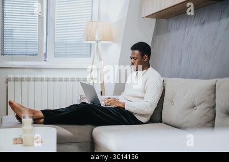 Uomo che indossa un pullover che lavora su un notebook comodo nel suo salotto Foto Stock