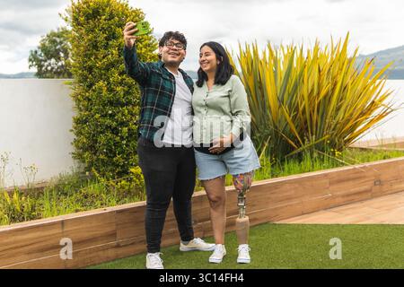 Coppia felice che fa un selfie nel loro giardino, celebra la gravidanza e mostra diversità Foto Stock