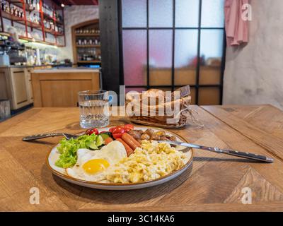 Abbondante piatto per la colazione con uova strapazzate, salsicce, patate arrostite, verdure fresche e cestino di pane croccante Foto Stock